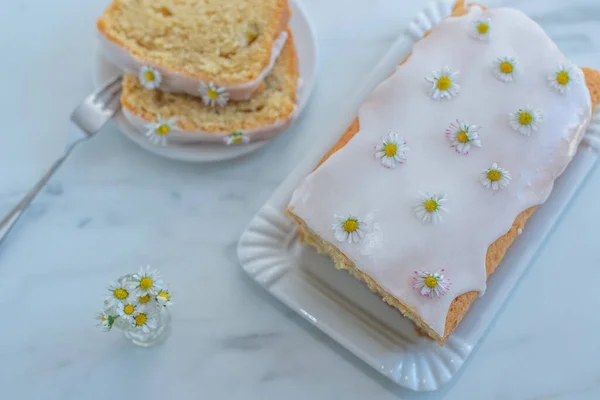 Ein Zitronenkuchen Mit Weißem Zuckerguss Und Gänseblümchen Auf Einem Marmortisch — Stockfoto