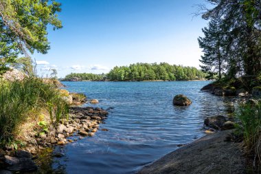 Göle bakan kayalık bir arazide güneşli bir günün dikey görüntüsü. İsveç yürüyüşü, doğa yürüyüşü