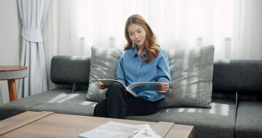 Evde dergi okuyan genç bir kadının portresi. Oturma odasındaki kanepede otururken moda dergisinin sayfalarını çeviren çekici bir kız.