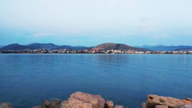 Bulutlu gökyüzünün altında güzel bir dağ, kaya ve deniz manzarası.