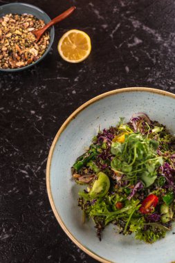 Farklı yeşillikli bir tabak salata, limon dilimi ve bir kase fındık..