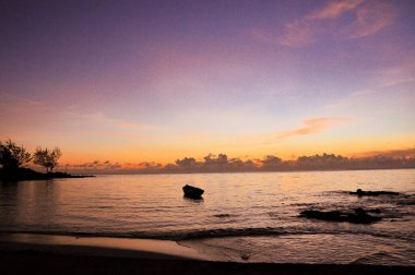 Güneşin batışıyla renklenen gökyüzünün arka planında yüzen bir kayıkla güzel bir deniz.