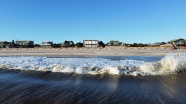 Deniz manzarası kıyıdaki binalara ve mavi gökyüzüne karşı dalgalanır..