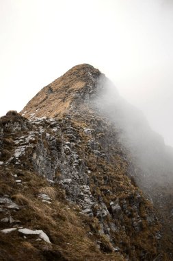 Swizterland 'da kar ve sisle kaplı dağın kayalık zirvesinin dikey görüntüsü.