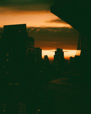 Günbatımında modern binalarla dolu bir şehir manzarasının silüeti.