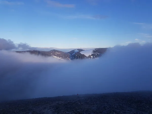 A scenic shot of a mountain that peaks through clouds during the sunrise