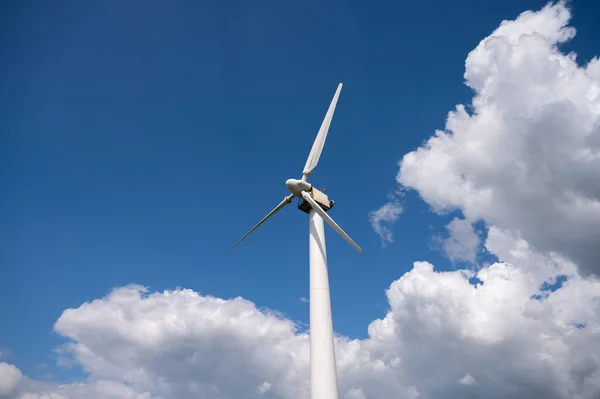 A low angle of wind turbine\'s giant propellers under the cloudy blue sky