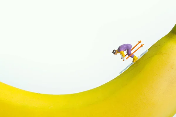 白い背景に隔離されたバナナの上を滑降するスキーヤーコンセプト 生の食べ物や運動を通して健康的にフィットします — ストック写真