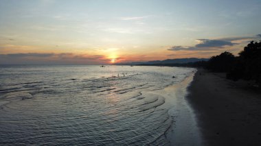 Gün batımında sahili yıkayan sakin dalgalarla baştan çıkarıcı Bayawan sahilinin insansız hava aracı görüntüsü.