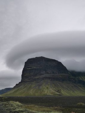 İzlanda 'da bulutlu bir gökyüzüne karşı yeşil bir dağın dikey görüntüsü.