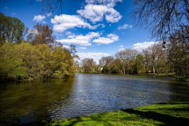 Macaristan 'da bulutlu gökyüzünün altında ağaçlar ve yeşil manzaralarla çevrili güzel bir göl.