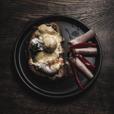 Tahta bir masada izole edilmiş siyah bir tabakta leziz bir yemeğin üst görüntüsü.