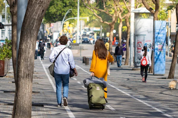 Barselona, İspanya - 29 Nisan 2022: Halka açık yolda yeşil bir bavulla yürüyen iki kız, seyahat kavramı.