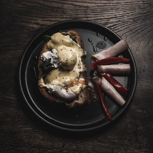 Tahta bir masada izole edilmiş siyah bir tabakta leziz bir yemeğin üst görüntüsü.