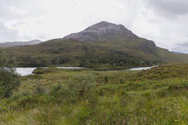 Bulutlu gökyüzünün altında nehir ve dağlar olan güzel bir manzara.