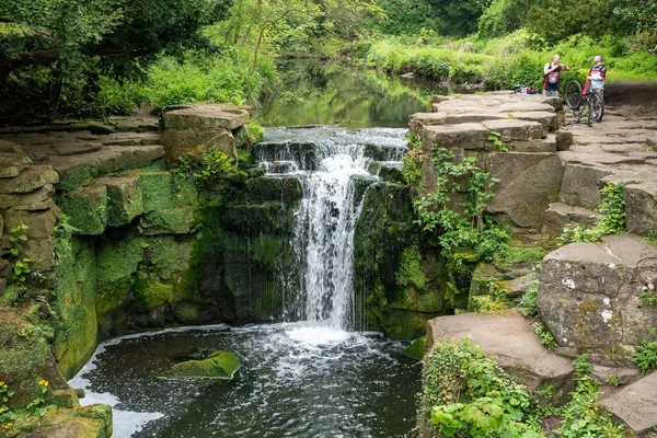 Two cyclists stop off at a waterfall, in Jesmond Dene, Newcastle upon Tyne, UK, for a rest. Concept of taking a break.