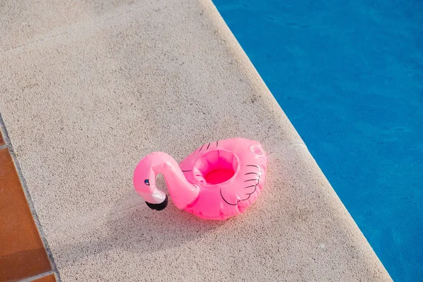 small pink flamingo float deflated on the edge of a swimming pool, summer time