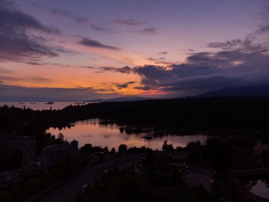 Ufukta gün batımı ve bulutlu gökyüzü olan ormanın ortasındaki küçük bir gölün nefes kesici görüntüsü.
