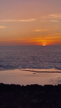 Günbatımında Atlantik Okyanusu 'nun dikey bir videosu, ufuktaki güneş gökyüzünü ve turuncu dalgaları boyadı.