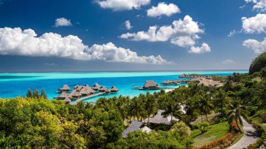 Conrad Bora Bora Nui otelinin mavi bulutlu gökyüzünün altında deniz aşırı bungalovları olan hava manzarası.