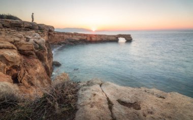 Gün batımında kayalık sahilde bir adam