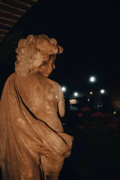 A vertical shot of an angel statue at night in a dark background