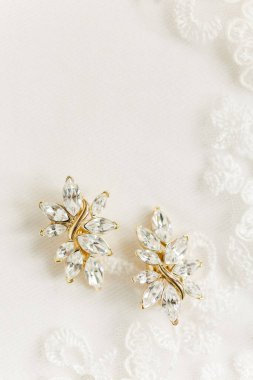 Beyaz dantelli arka planda elmas işlemeli 2 yaprak şeklinde altın küpeler.