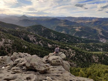 Dağlarda bir kayanın kenarında oturan bir adam