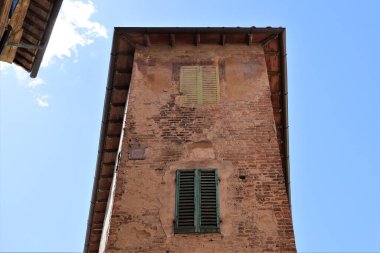 Mavi duvarlı ve mavi gökyüzüne bakan yeşil pencereli eski bir taş binanın alçak açılı görüntüsü.