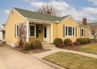 Yuvarlak şekilli çalı bahçeli modern sarı ayrık bir evin dış cephesi.