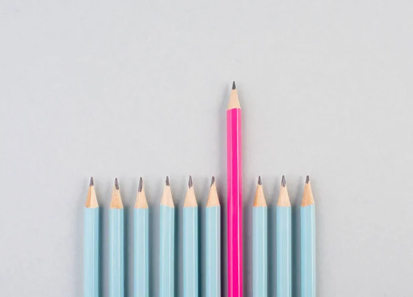 Blue pencils in a row, one pink pen is standing out, be different, leadership and teamwork concepts