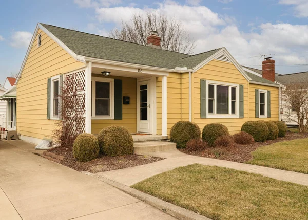 Yuvarlak şekilli çalı bahçeli modern sarı ayrık bir evin dış cephesi.