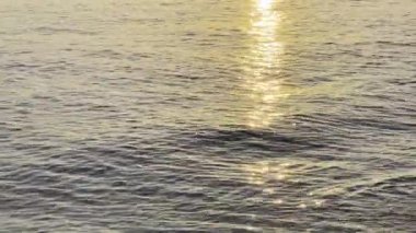 Sakin bir deniz suyu dalgaları ve parlak sarı güneş yansımaları.