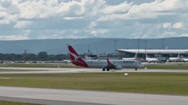 Qantas uçağının taksicilik, dönüş ve hızının görüntüsü. Havaalanı araçları hareket ediyor, arka planda tepeler, Batı Avustralya
