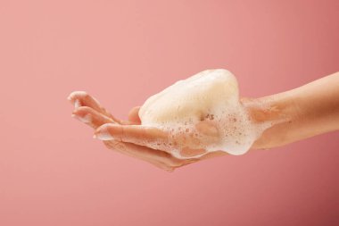 Parlak pembe arka planda sabun ve köpüklü ellerin yakın plan çekimi.