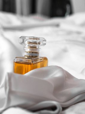 Beyaz ipek kumaş üzerinde portakal suyu olan sığ bir parfüm şişesi.