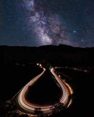 Yıldızlı bir gece gökyüzünün altında uzun süre araba izleri olan kıvrımlı bir yol.