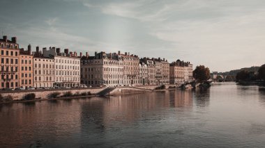 Bulutlu gökyüzünün altında ağaçların olduğu nehrin kenarındaki binaların güzel bir görüntüsü.