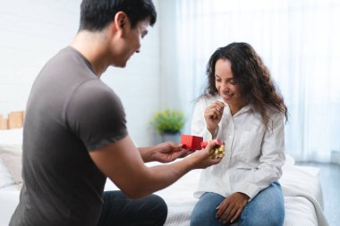 Taylandlı bir adam, yatak odasında bir kadına kırmızı hediye kutusu sunuyor.