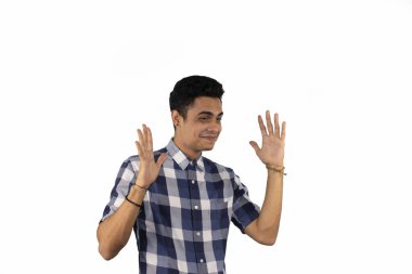 Mavi beyaz kareli gömlekli, elleri beyaz arka planda gülümseyen genç bir İspanyol erkek.