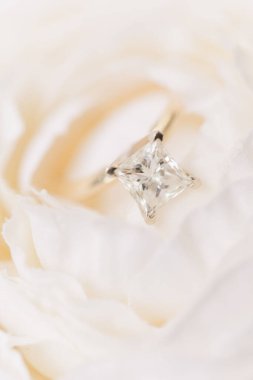 Beyaz bir çiçeğin üzerindeki elmas nişan yüzüğünün dikey yakın çekimi.