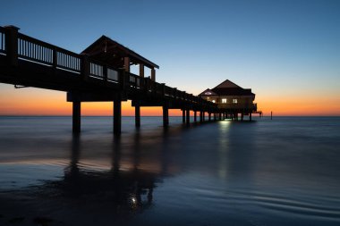 Manzaralı gün batımında deniz kenarında bir evin olduğu büyüleyici bir deniz manzarası.