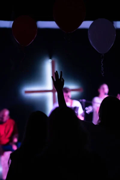 A vertical of a lifted hand during worship service led cross in the background