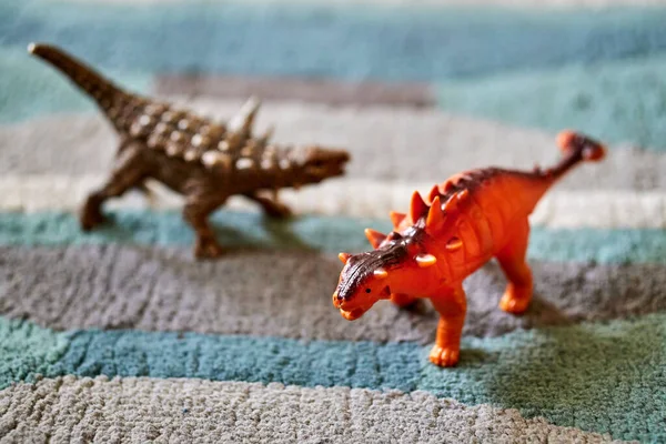 在明亮的灯光下 一个橙色的龙龙玩具在地毯上与另一个褐色恐龙玩具在模糊的背景下的特写镜头 — 图库照片