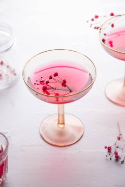 Kırmızı şarap kokteylinin dikey görüntüsü üzerinde çiçekler olan küçük bir dal ve şampanya kadehi.