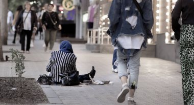 İnsanlar geçerken yolda oturup para dilenen bir insanın arka planı.