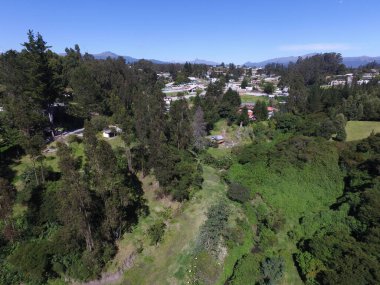 Güneşli bir günde yeşil ormanlarla kaplı tepelerin ve kırsal alandaki evlerin kuş bakışı görüntüsü