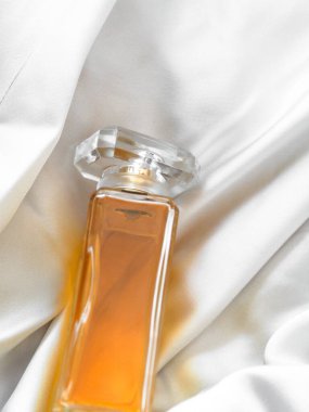 Beyaz ipek kumaş üzerinde portakal suyu olan sığ bir parfüm şişesi.