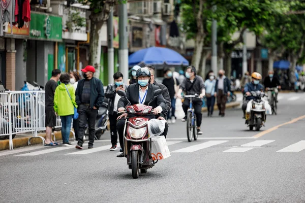Yüz maskeli insanların Şangay 'da scooter sürerken COVID19 tecrit karantinasında olduğu dikey bir fotoğraf.