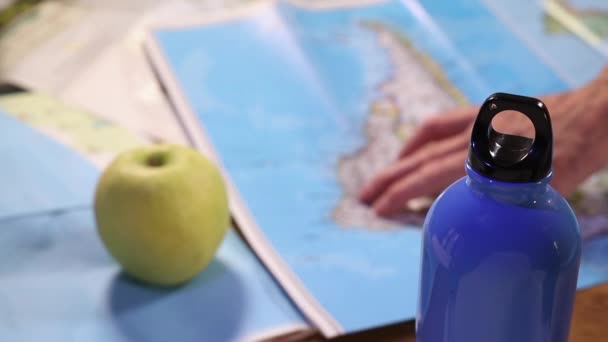 女性の手のポイントは 世界地図では 旅行計画のための地図を研究し 前景の水のボトルで — ストック動画